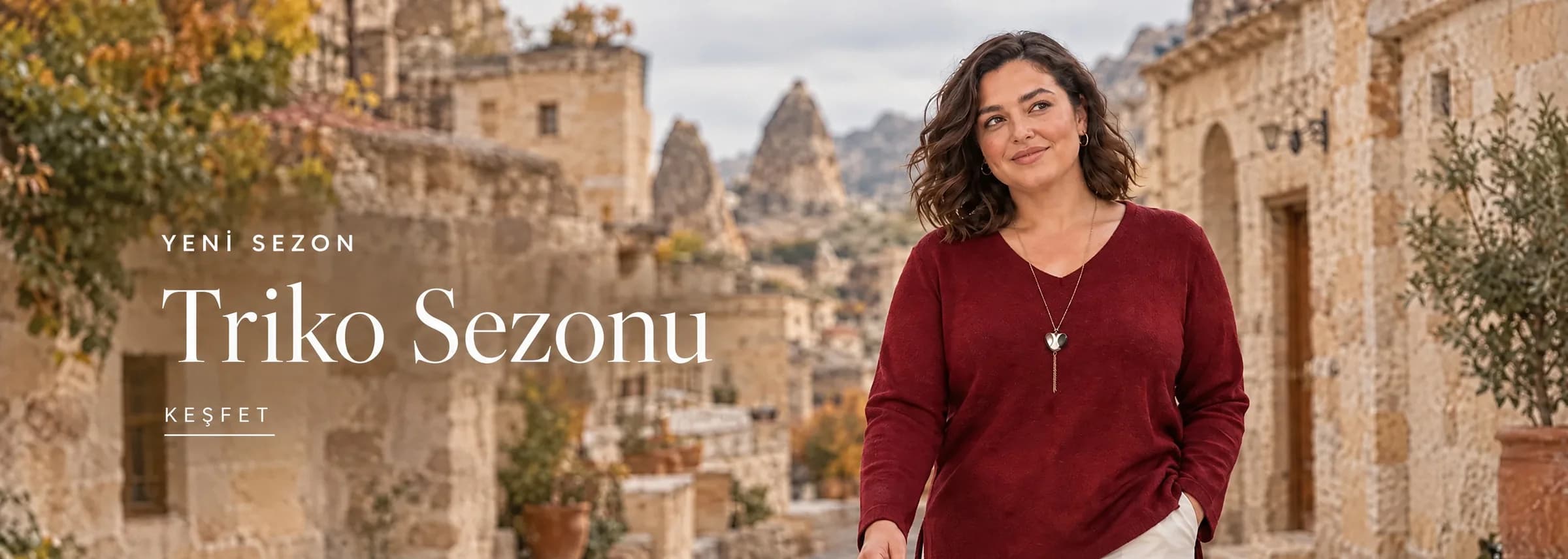 Tarzım Süper açılış görseli: Kapadokya'da taş evlerin önünde bordo triko bluz ve kolye takan model; solda Yeni Sezon Triko Sezonu yazısı ve Keşfet bağlantısı.