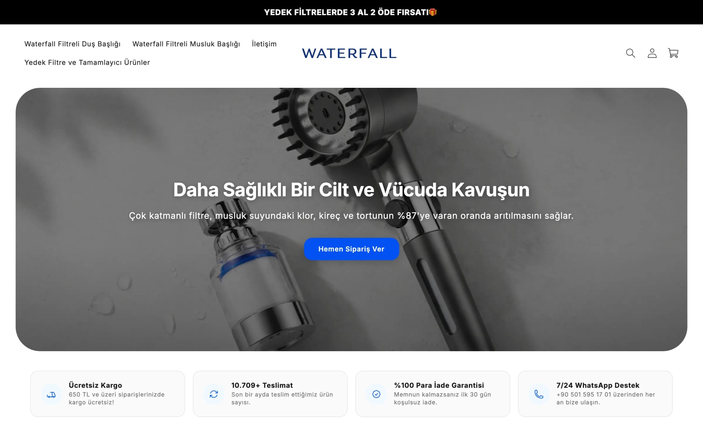 Waterfall'ın masaüstü ana sayfası: üstte siyah şeritte Yedek filtrelerde 3 al 2 öde fırsatı, solda Waterfall Filtreli Duş Başlığı, Waterfall Filtreli Musluk Başlığı, İletişim ve Yedek Filtre ve Tamamlayıcı Ürünler menüsü, ortada lacivert WATERFALL logosu; yuvarlak köşeli açılış alanında ıslak gri zeminde duş başlığı ve filtreli musluk başlığı fotoğrafı üzerinde Daha Sağlıklı Bir Cilt ve Vücuda Kavuşun başlığı, %87 arıtma cümlesi ve mavi Hemen Sipariş Ver düğmesi; altta ücretsiz kargo, teslimat sayısı, para iade garantisi ve WhatsApp destek kartları.