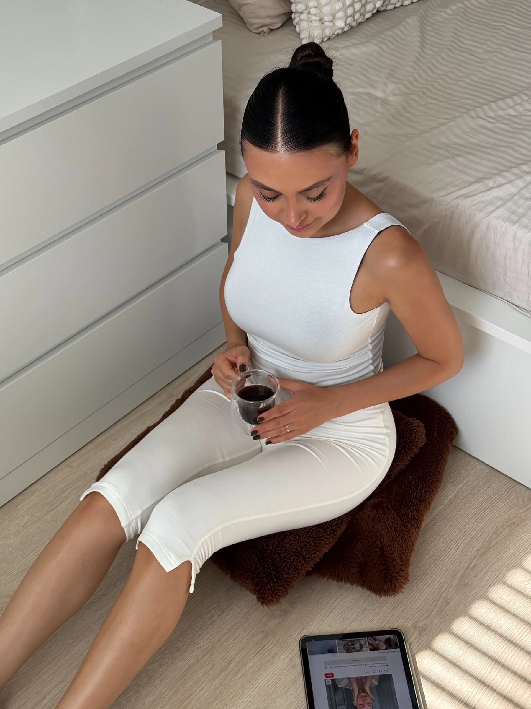 Deep Dual atletin cream yüzü: kahverengi tüylü halının üzerinde yerde oturan, elinde kahve bardağı tutan model; yanında tablet.