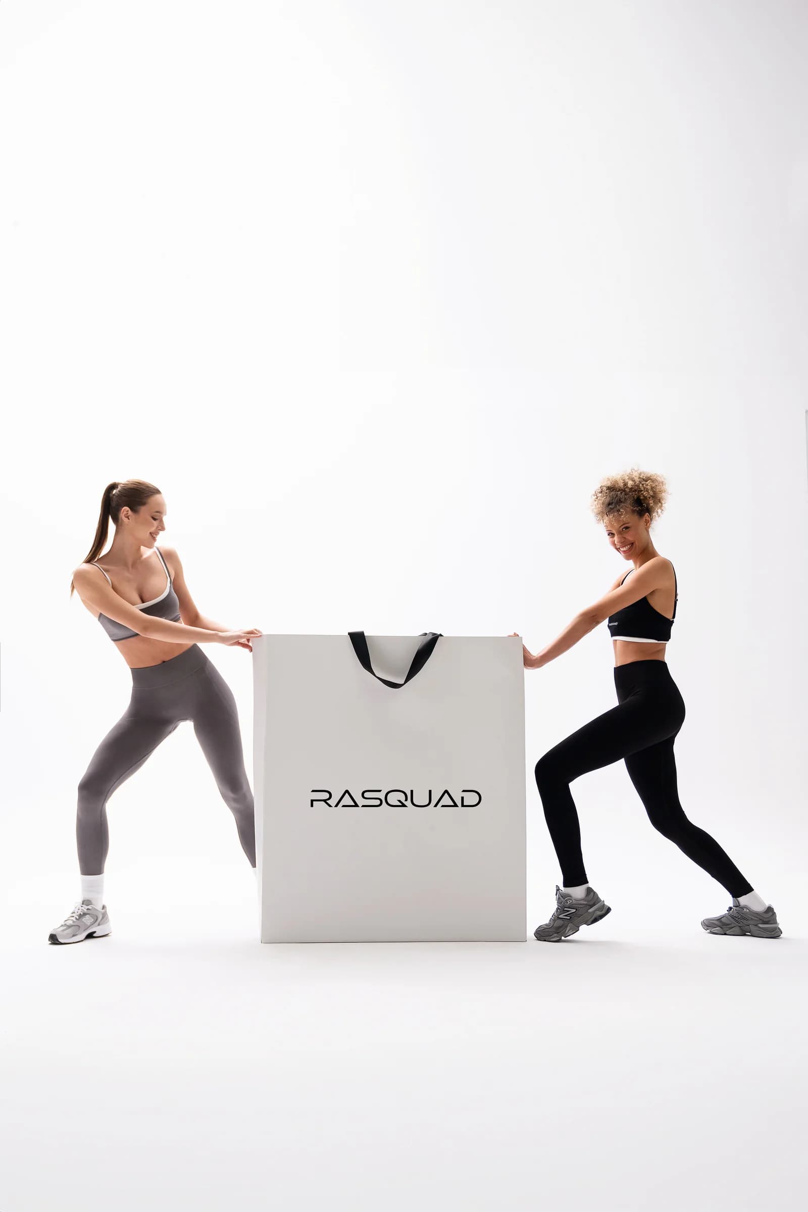 Rasquad Last Pieces görseli: beyaz stüdyoda ortadaki büyük, RASQUAD logolu alışveriş çantasını iki yandan çeken, gri ve siyah tayt giyen iki model.