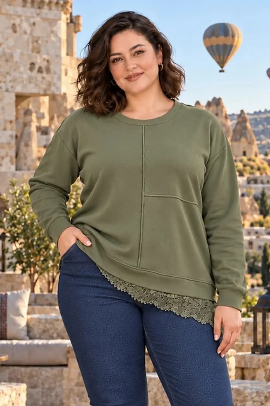 Tarzım Süper Sweatshirt kategori görseli: arkada sıcak hava balonu ve taş evler, eteği dantel detaylı yeşil sweatshirt ve kot pantolon giyen model.